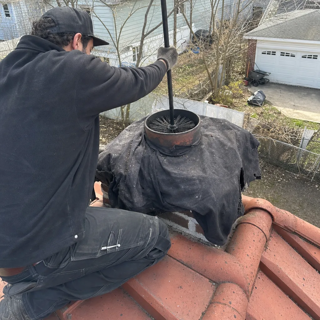 Professional chimney sweep cleaning a chimney flue on a rooftop.