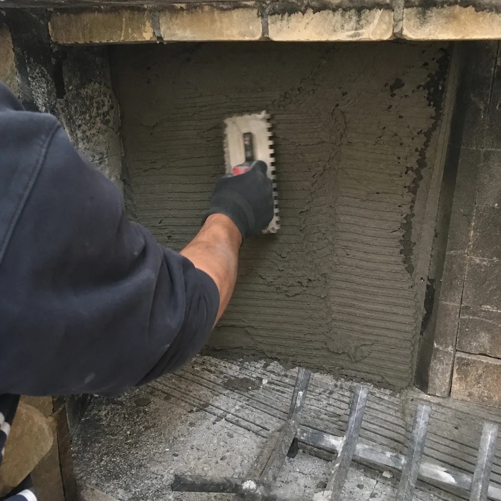 Worker applying mortar with a notched trowel to a fireplace wall in Brooklyn, NY